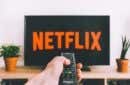 person holding a remote control pointed at a TV displaying the Netflix logo - a-person-holding-a-remote-control-pointed-at-a-TV-displaying-the-Netflix-logo